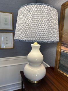 a white lamp sitting on top of a wooden table next to a framed painting and pictures