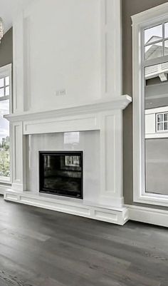 an empty living room with two windows and a fireplace in the center, surrounded by wood flooring