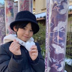 a young boy wearing a black hat and coat standing next to a tall purple pole