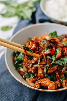 a white bowl filled with stir fry chicken and spinach next to chopsticks