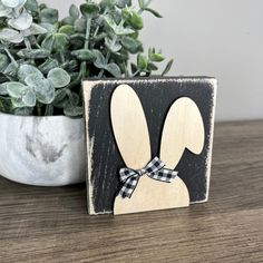 a wooden bunny with a bow on it's head sitting next to a potted plant