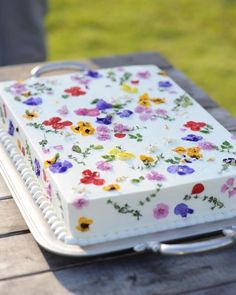 a cake with flowers on it sitting on top of a wooden table next to a knife