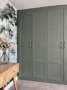 a room with green cupboards and flowers on the table in front of wallpaper