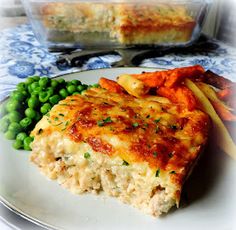 a white plate topped with lasagna and green peas next to a casserole dish