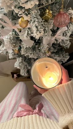 a person holding a lit candle in front of a christmas tree with ornaments on it