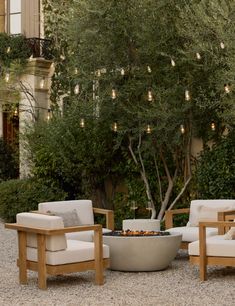 two chairs and a fire pit in front of a tree with lights hanging from it