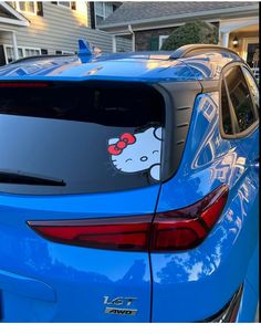 a blue car with a hello kitty sticker on it's rear window is parked in front of a house