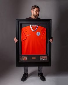 a man holding up a framed soccer jersey in front of his face and looking at the camera