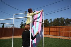 two people standing on top of a pink and blue surfboard in a metal frame