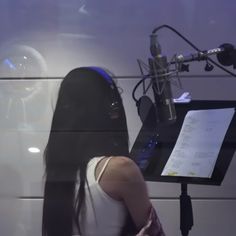 a woman sitting in front of a microphone with her head resting on a desk next to a sheet of paper