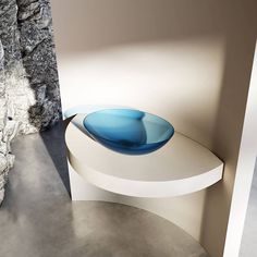 a blue glass bowl sitting on top of a white table next to a stone wall