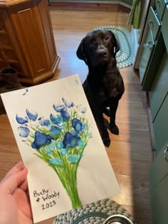 a black dog sitting on the floor next to a greeting card with blue flowers in it