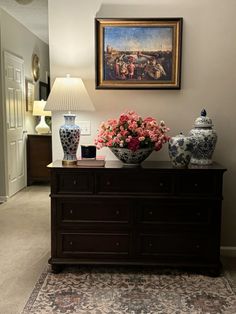 vases and flowers sit on top of a dresser in a room with a painting above it