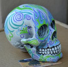 a colorful painted skull sitting on top of a cardboard box next to a piece of paper