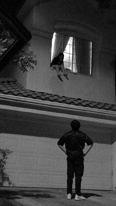 a person standing in front of a house with a dog jumping up into the air