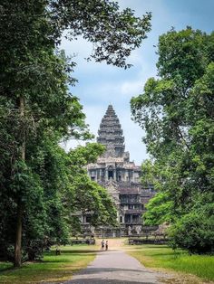 an ancient building in the middle of trees and people walking down it's path