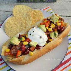 a hot dog with toppings on a plate next to tortilla chips