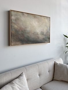 a painting hanging on the wall above a couch in a living room with a potted plant