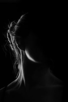 a black and white photo of a woman's face in the dark with her hair pulled back