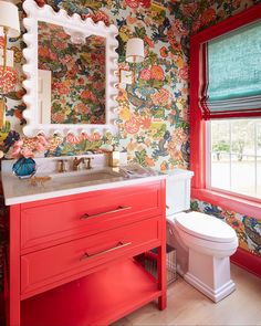 a bathroom with colorful wallpaper and red cabinetry, toilet and sink in the foreground