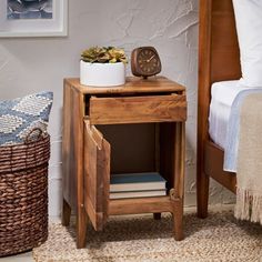 a small wooden table with a clock on it next to a basket and bedding