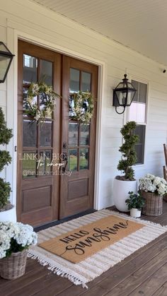 a welcome mat on the front porch of a house with wreaths and potted plants