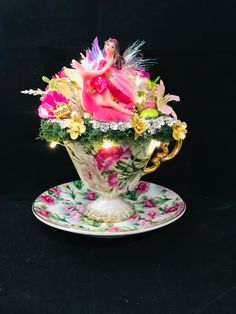 a teacup with flowers and fairy figurines in it on a black background