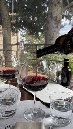 two glasses of red wine being poured into them on a table with plates and utensils