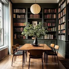 a dining room table surrounded by bookshelves with chairs and a vase filled with flowers