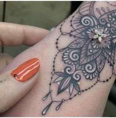 a woman's hand with an orange manicure on it and a tattoo design