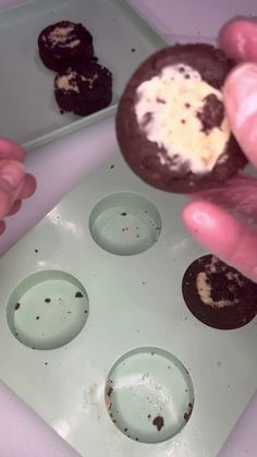 a person is picking up an oreo cookie from a tray with four holes in it