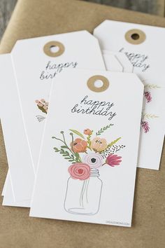 four tags with flowers and happy birthday written on them are sitting on a brown envelope