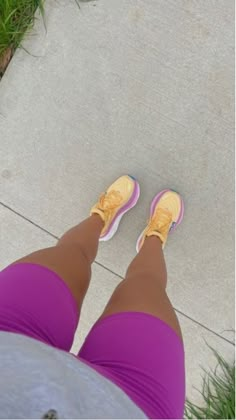 a woman's legs with yellow and pink shoes standing on the sidewalk next to grass