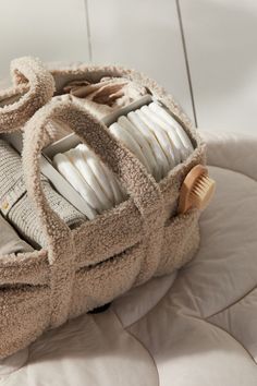 a pile of white dishes sitting in a basket on top of a bed next to a pillow