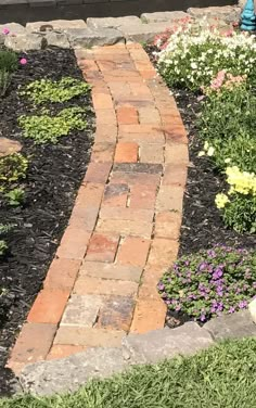 a brick path in the middle of a flower garden