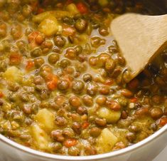 peas and potatoes are being cooked in a pot with a wooden spoon on the side