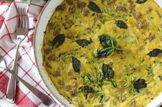 an omelet with spinach and sausage in a white dish on a red checkered table cloth