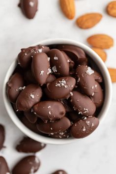 chocolate almonds in a white bowl on a marble surface with almonds scattered around