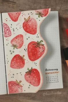 an open notebook with strawberries on it next to markers and marker pens, along with a calendar