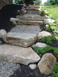 a garden with rocks and plants in the middle, along side a house that has a stone walkway leading up to it