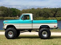 a blue and white truck parked on top of a grass covered field next to a lake