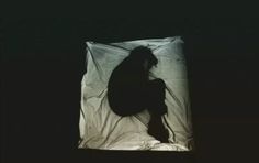 a black and white photo of a person sitting on a sheet in the dark,