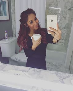 a woman is taking a selfie in the bathroom with her coffee cup and cell phone