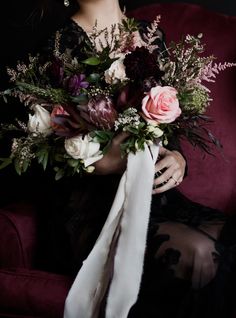 a woman sitting on a red couch holding a bouquet of flowers and greenery in her hands