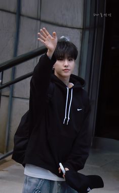 a young man with his hand up in the air while wearing a black hoodie