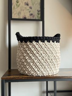 a woven basket sitting on top of a wooden table next to a framed painting and chair