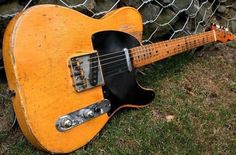 an old yellow guitar laying on the ground next to a chain link fence