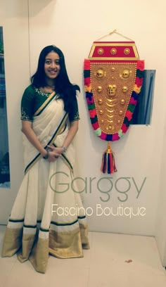 a woman in a white sari standing next to a wall hanging on the wall