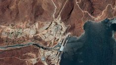 an aerial view of a large body of water next to a mountainous area with buildings