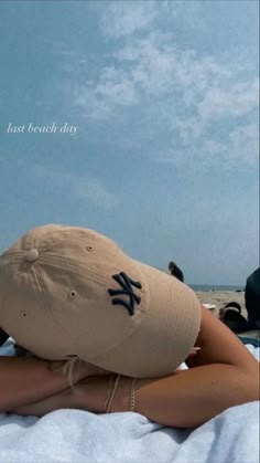 a woman laying on top of a beach next to the ocean wearing a baseball hat